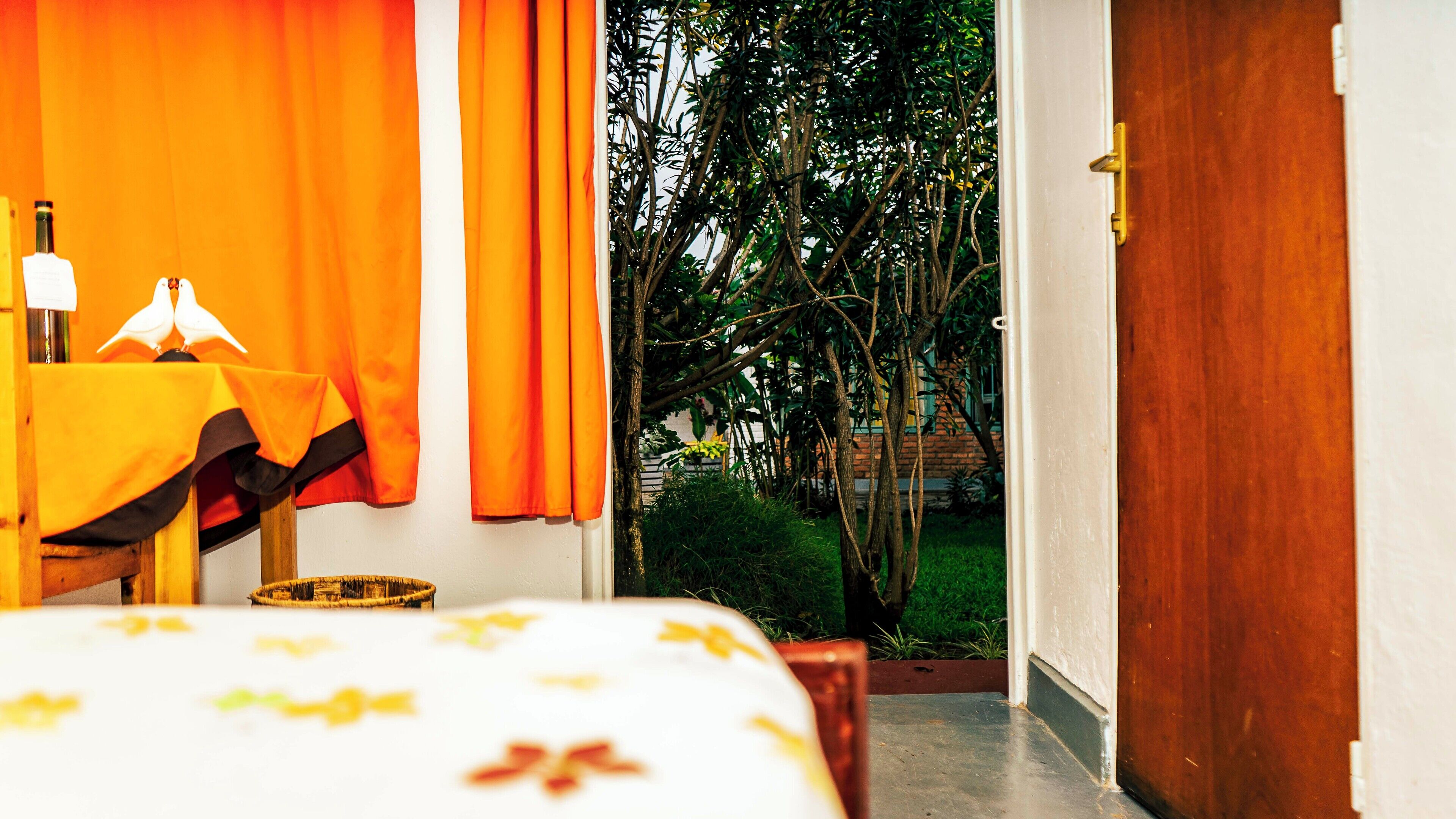 A room with a bed, a table with a lamp, and a view of a garden through an open door.