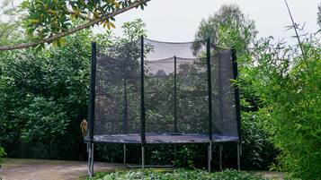 Un trampolín con red de seguridad, rodeado de follaje denso.