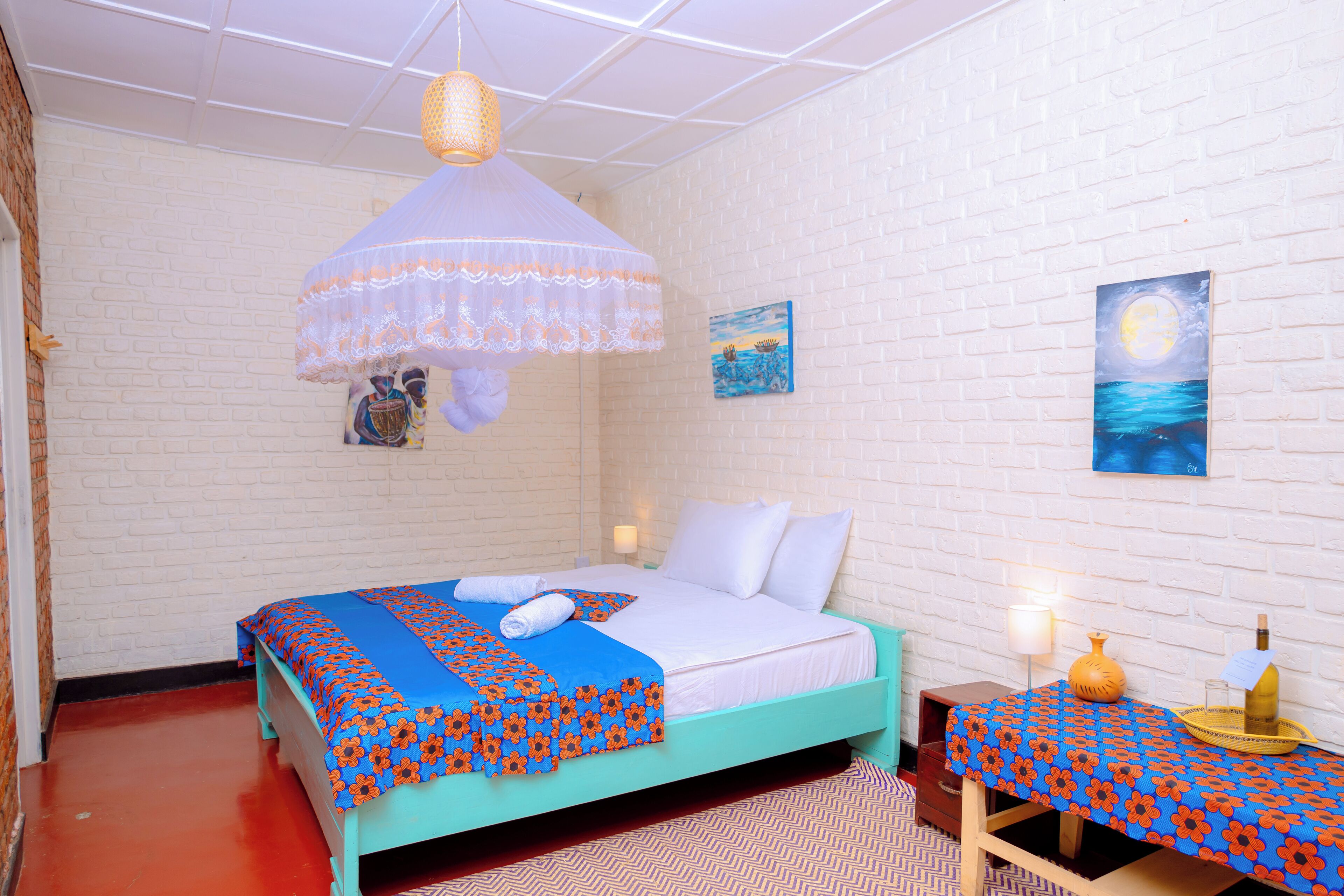 A room with a bed, a table with a bottle and a tray, and a wall with a painting.