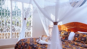 Una cama con dosel, ropa de cama estampada y una vista a través de una ventana con celosías metálicas decorativas.