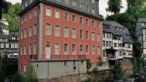 A red brick building with multiple windows, a stone base, and a river in front.