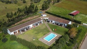 Vue aérienne d’une propriété résidentielle dotée d’une piscine, de plusieurs bâtiments et d’un espace vert environnant.