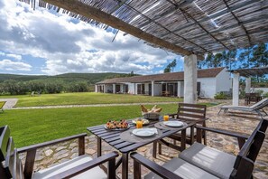 Enjoy a meal in a serene outdoor setting with a pergola providing shade and a beautiful lawn view.