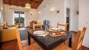 A dining area with a wooden table set for two, a sofa, and a view of the outdoors. - Burro Ville - Serene Houses w/ Pool by HostWise (Portimão)
