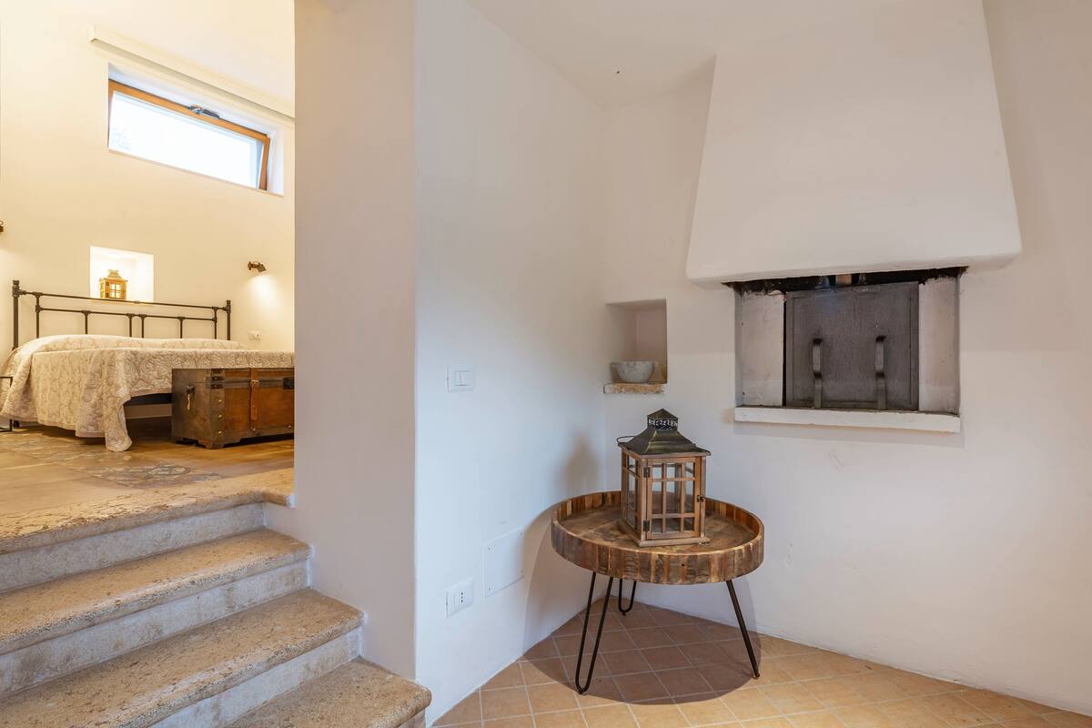 Un dormitorio con una cama, una mesita de noche y una ventana. Se ve una escalera que lleva a otra habitación.