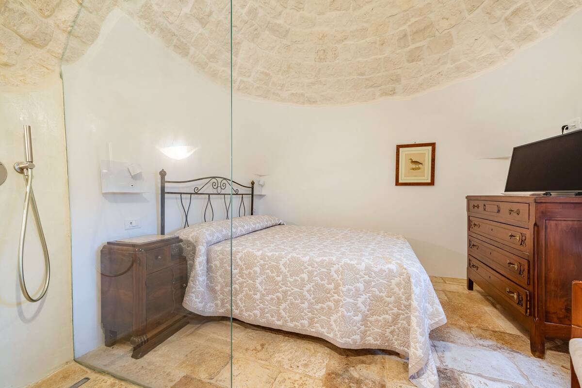 Un dormitorio con cama, cómoda de madera y televisor sobre un mueble.