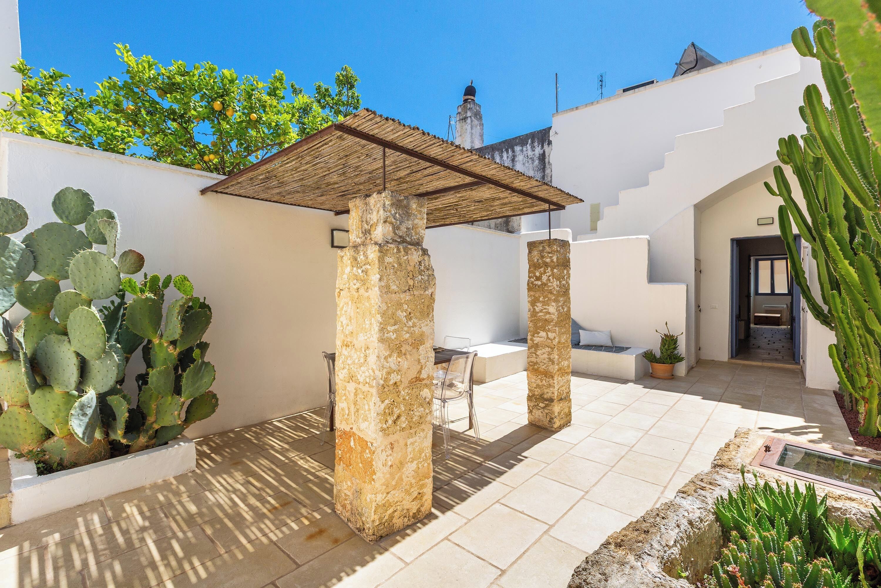 Ein Innenhof mit einer Pergola, Kakteen, steinernen Säulen und einem Fliesenboden.