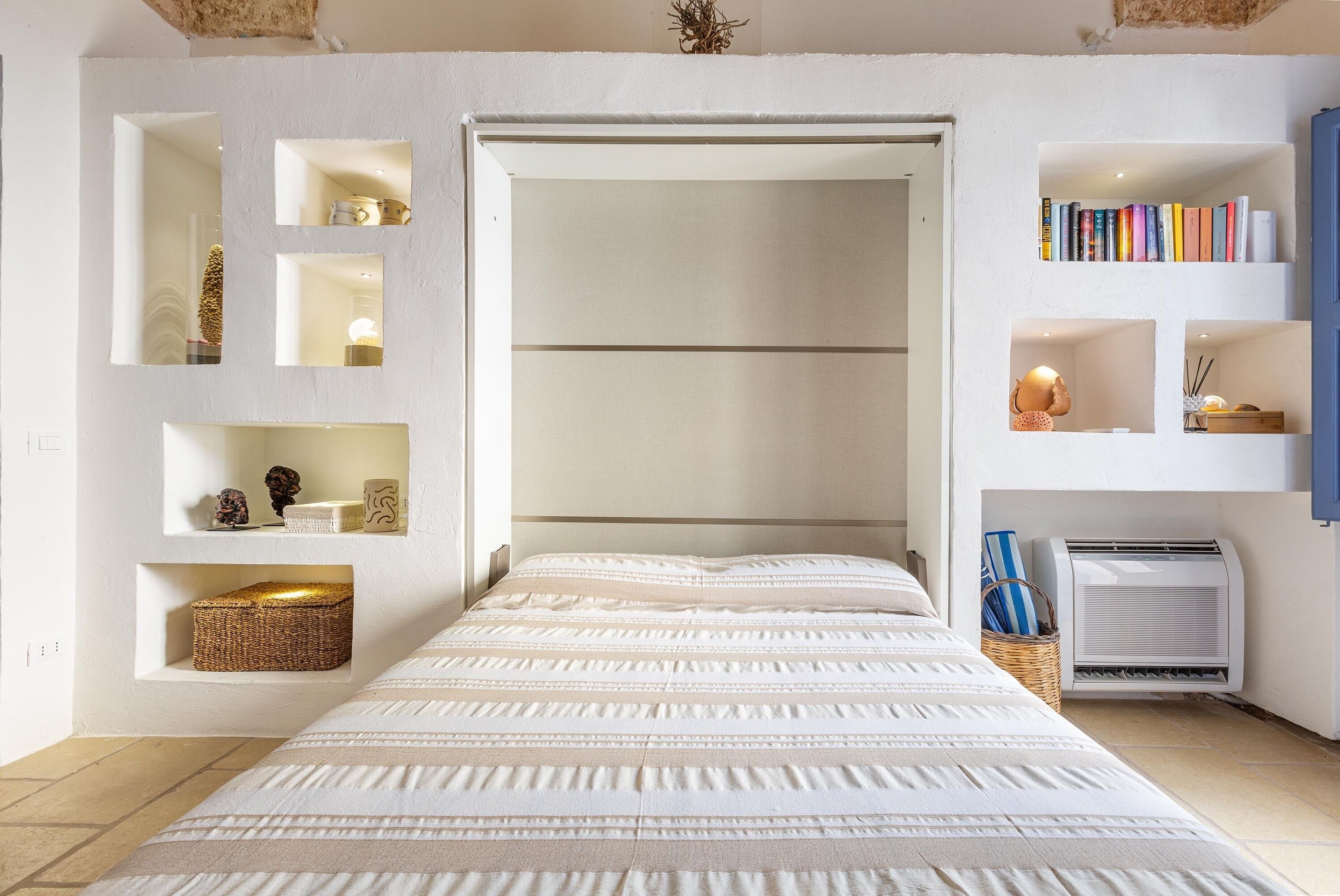 Un dormitorio con cama, estanterías empotradas, una mesita pequeña y aire acondicionado de pared.