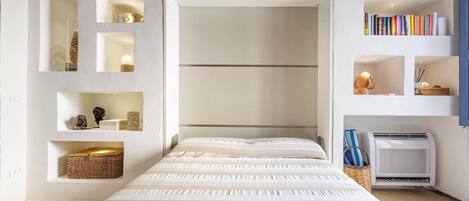 Un dormitorio con cama, estanterías empotradas, una mesita pequeña y aire acondicionado de pared.