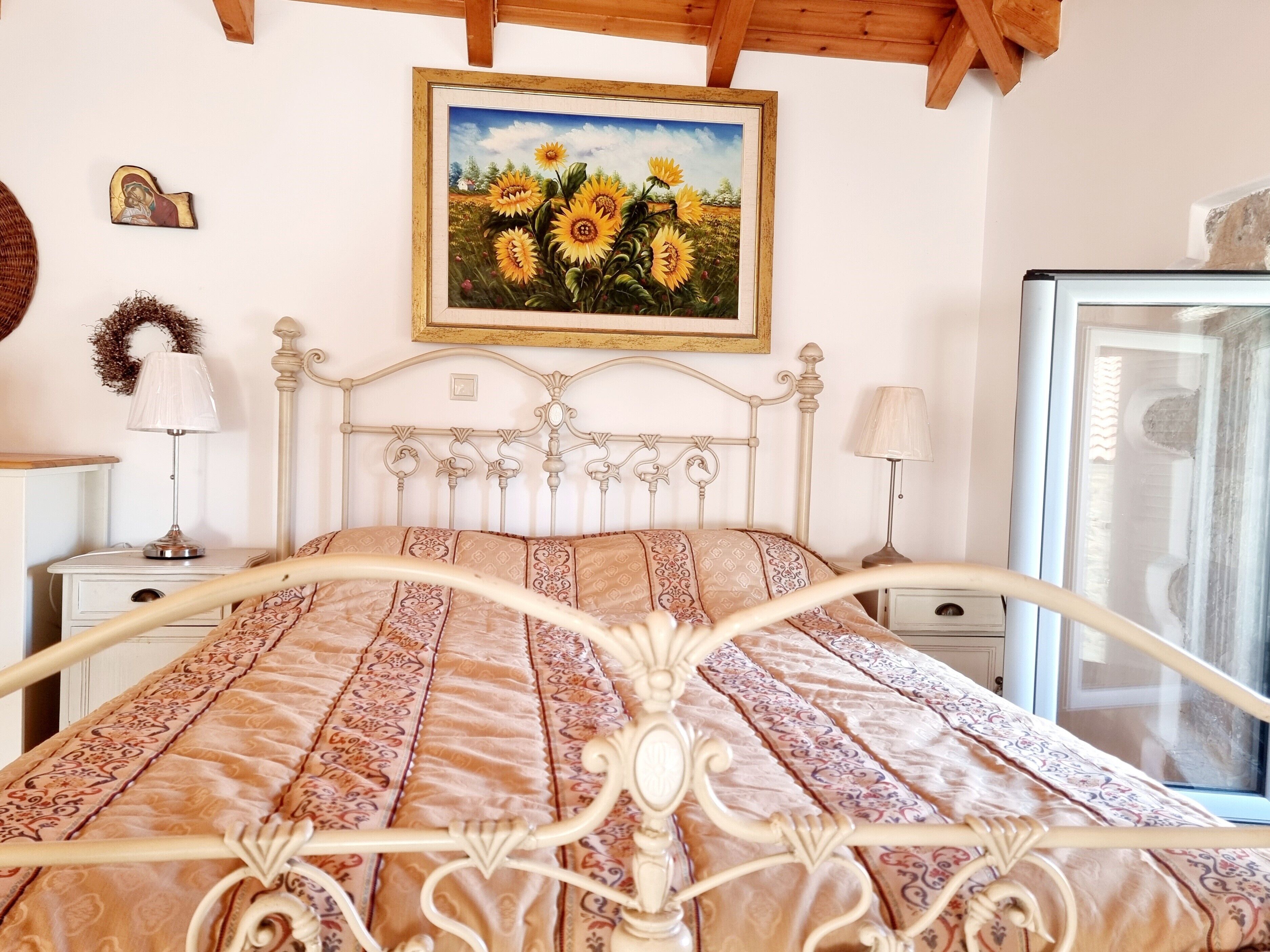 Quarto com cama, mesa de cabeceira, abajur, pintura de girassóis e televisão.