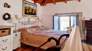 Un dormitorio con techo de madera, una cama con ropa de cama estampada, una mesita de noche con lámpara, un aparador y una ventana con vistas al exterior.