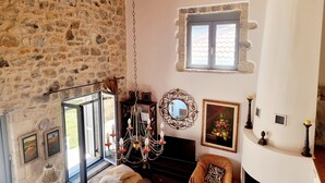 Una habitación acogedora con pared de piedra, techo de madera, candelabro, chimenea y ventana con vistas.