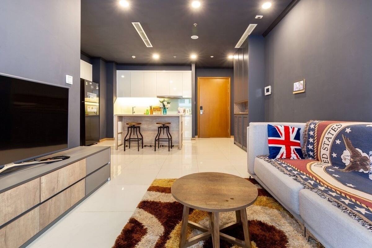 A modern living room with a sofa, a TV, a coffee table, and a kitchen in the background.