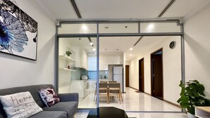 A modern living room with a sofa, a coffee table, and a kitchen visible through a glass door. - SaigonHomes in Vinhomes Central Park (Ho Chi Minh City)