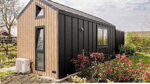 A modern, single-story building with a wooden exterior and a black roof. - Description (Waarde)