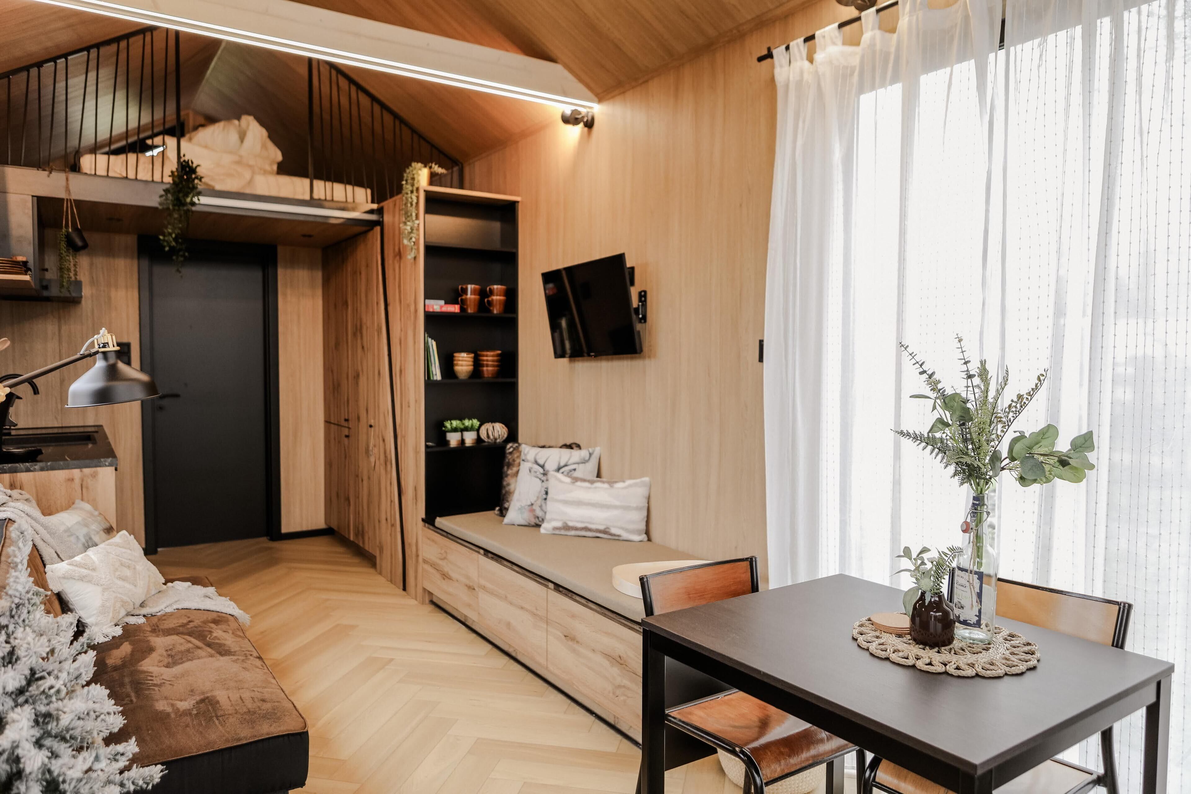 Ein gemütliches Zimmer mit einer Holzbank, einem Esstisch und einem an der Wand befestigten Fernseher.