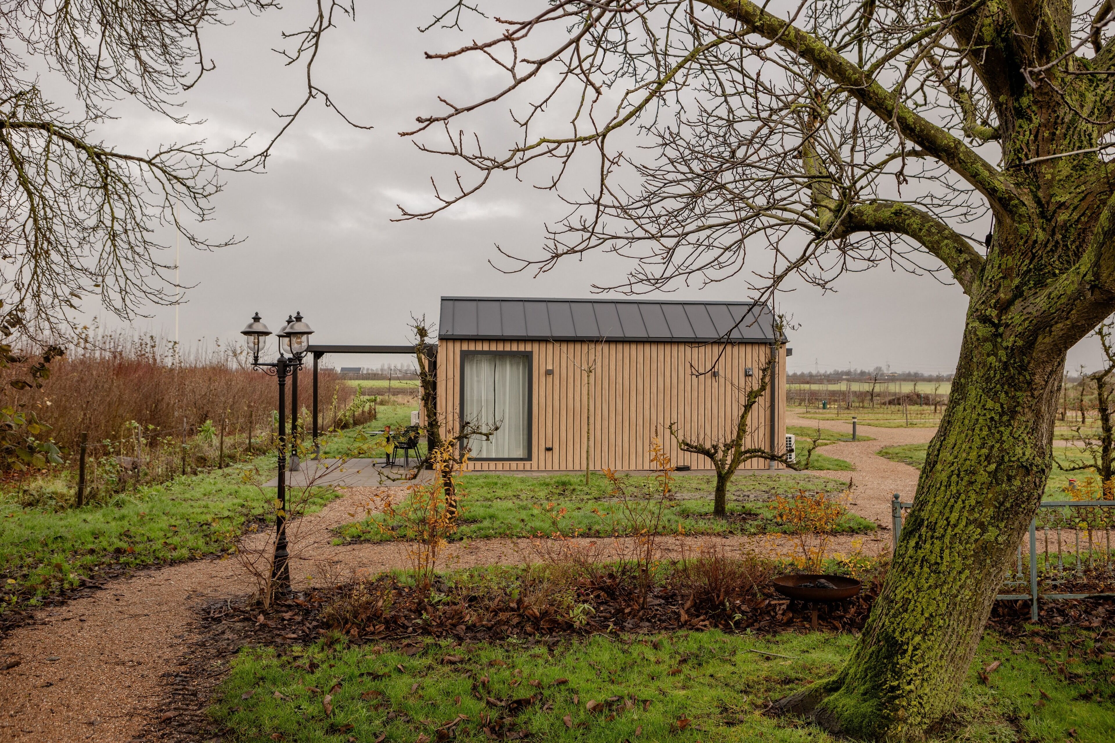 Een klein houten gebouw met een deur en ramen, omgeven door gras en bomen.