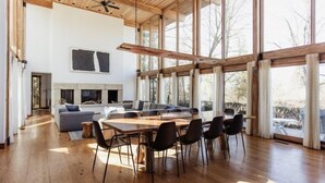 A spacious living area with a large wooden dining table, black chairs, a grey sofa, and a fireplace.