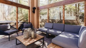 A modern living room with a sofa, two chairs, a coffee table, and large windows offering a view of a forested area.