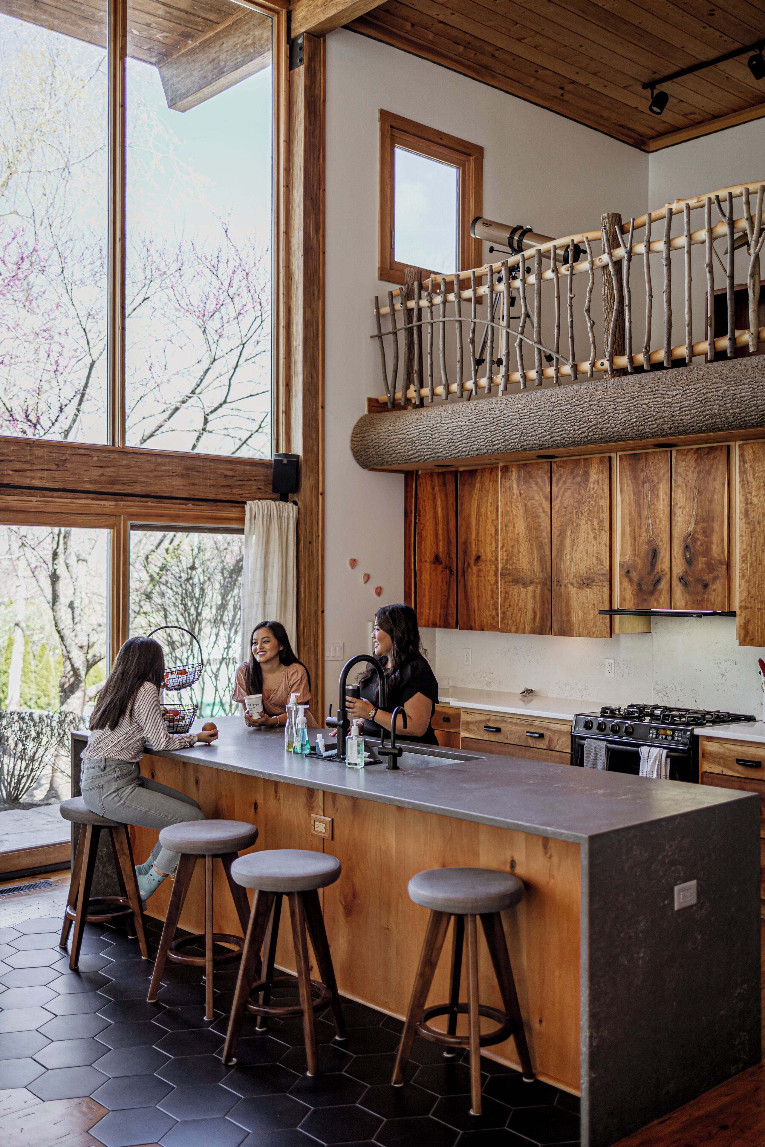 Una cocina moderna con armarios de madera, una isla grande con taburetes y vistas a árboles.