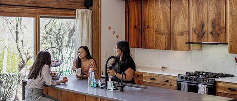 Una cocina moderna con armarios de madera, una isla grande con taburetes y vistas a árboles.