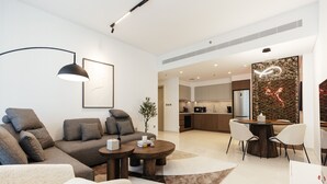 A modern living room with a sectional sofa, a coffee table, and a dining area with a wooden table and chairs. - Luxurious Waterfront 1BR with Sea Views (Dubai)