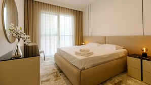 A modern hotel room with a large bed, a bedside table with a lamp, a mirror, and a vase with flowers. - Luxurious Waterfront 1BR with Sea Views (Dubai)