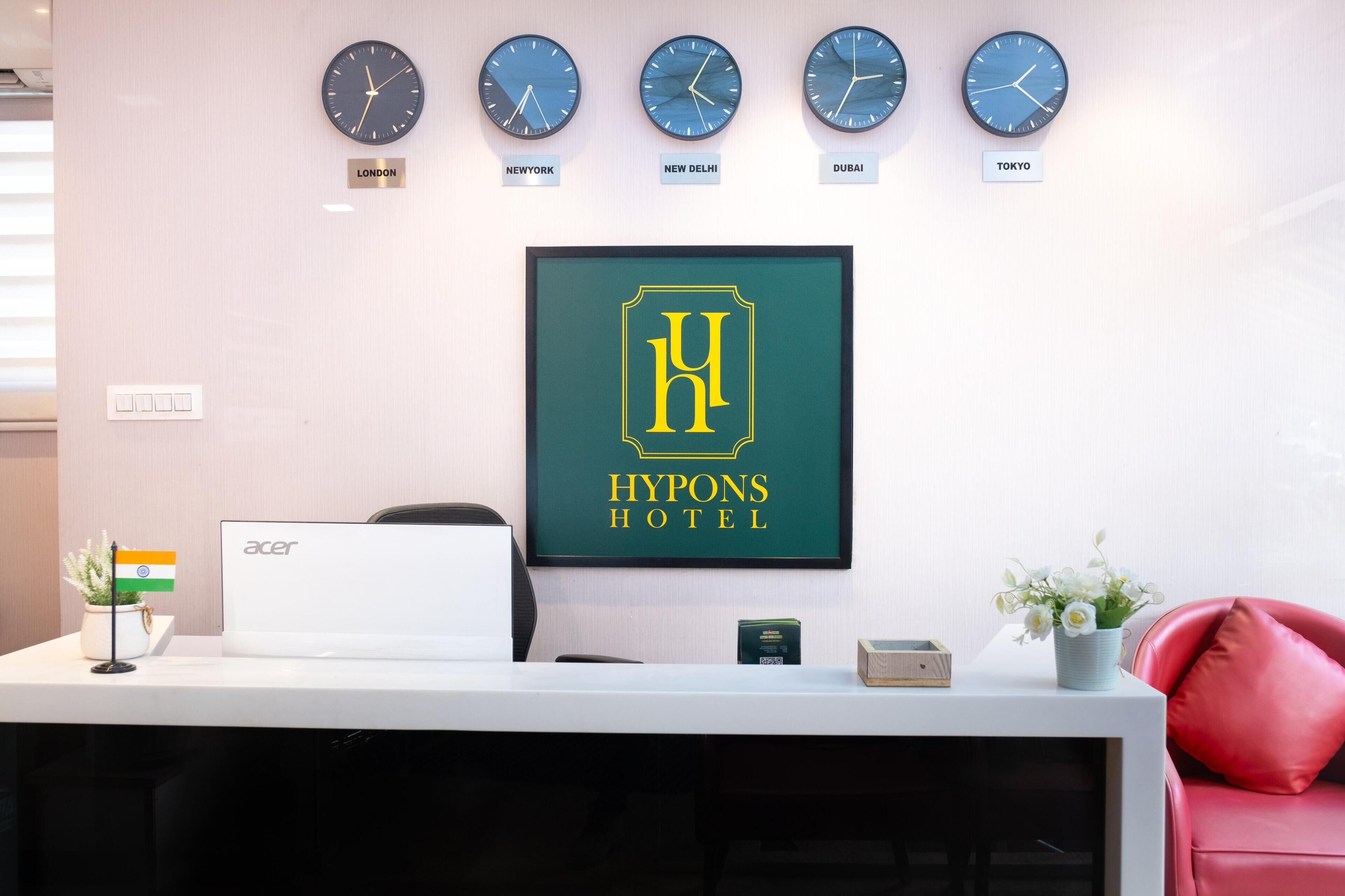A reception desk with clocks showing different time zones, a framed hotel logo, and a laptop.