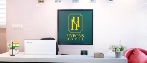 A reception desk with clocks showing different time zones, a framed hotel logo, and a laptop.