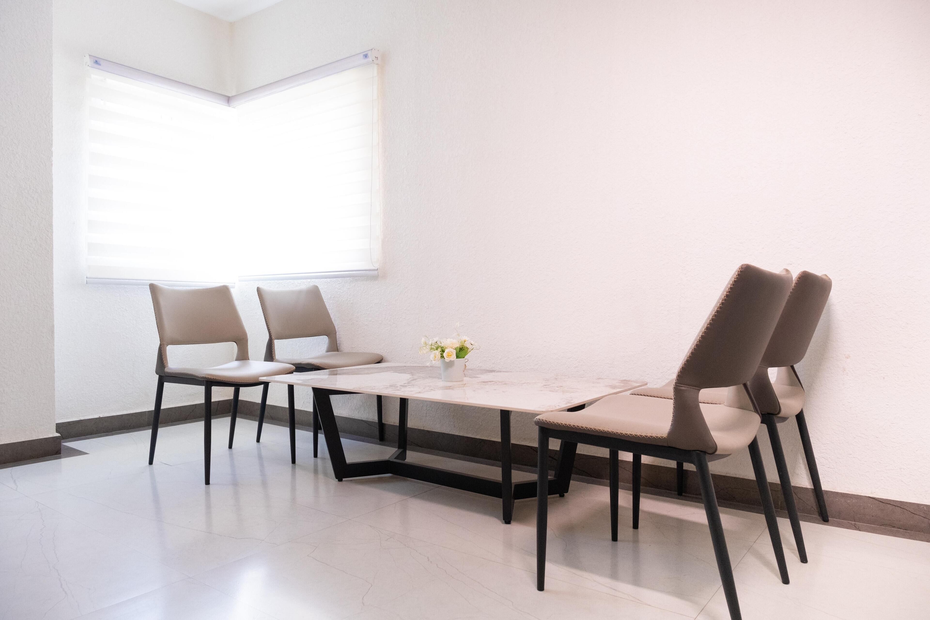 Un comedor moderno con una mesa blanca, cuatro sillas y un florero con flores.