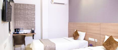 A hotel room with two beds, a desk, a chair, an air conditioning unit, and a television.