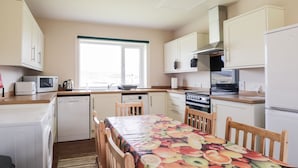 A compact kitchen with white cabinets, a microwave, a stove, and a sink. There's a window providing natural light and a table with chairs. - Loubcroy Farm House (Lairg)