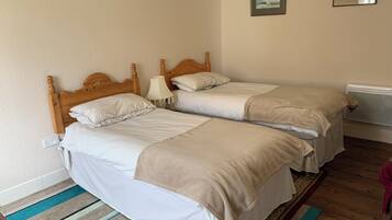 Una habitación con dos camas de madera, ropa de cama blanca, un tapete a rayas y un radiador.