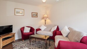 A living room with a flat-screen TV, two red sofas, a beige sofa, a patterned rug, and a table. - Loubcroy Farm House (Lairg)