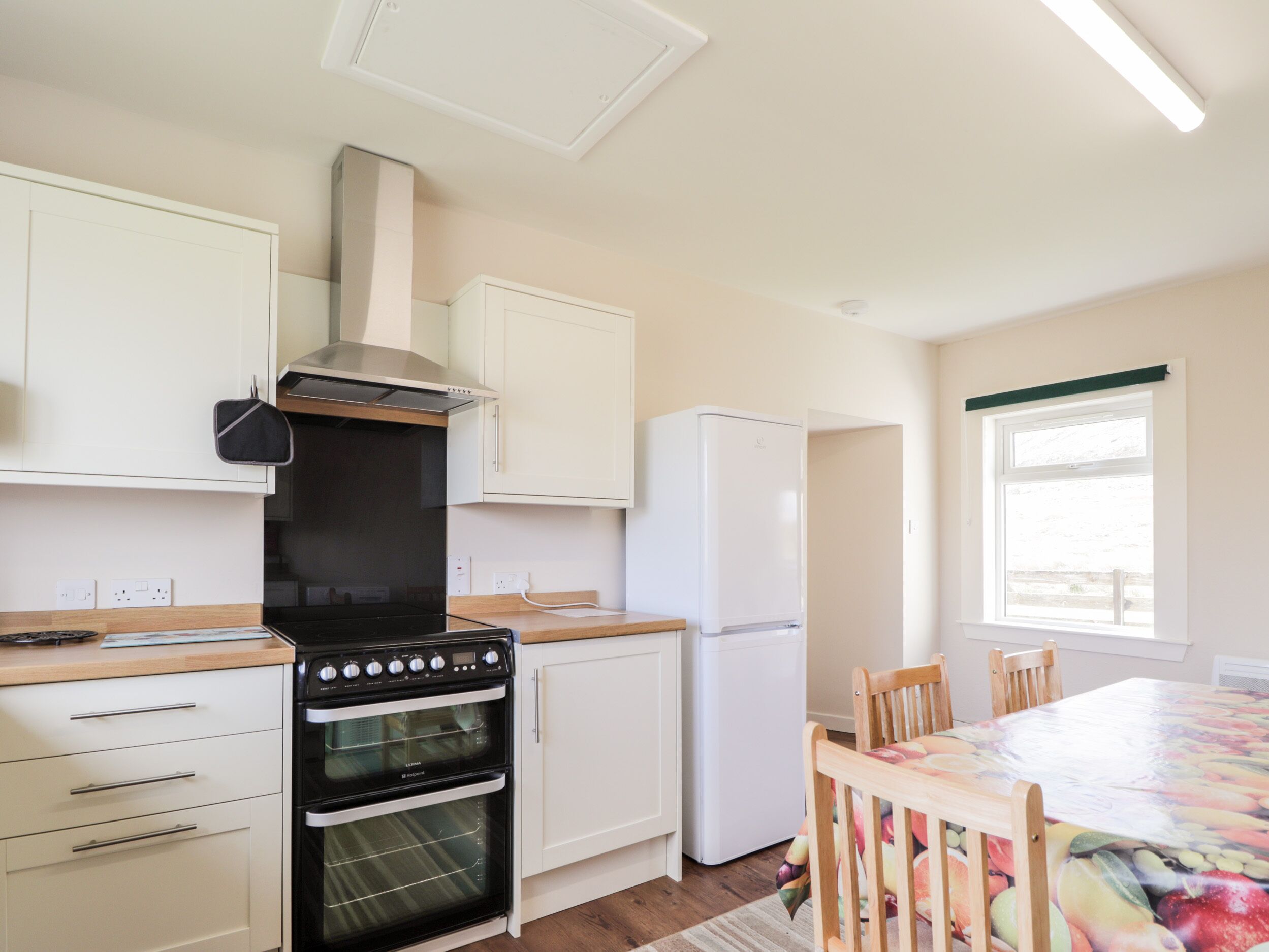 A kitchen with white cabinets, a black oven, a white refrigerator, and a wooden dining table with chairs.