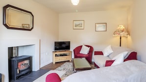 A cozy living room with a fireplace, a television, a red armchair, and a sofa. - Loubcroy Farm House (Lairg)