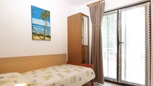 A bedroom with a bed, a nightstand, a lamp, a painting of a beach, a wardrobe, and a sliding glass door. - Holiday apartment with air conditioning (Banjole)