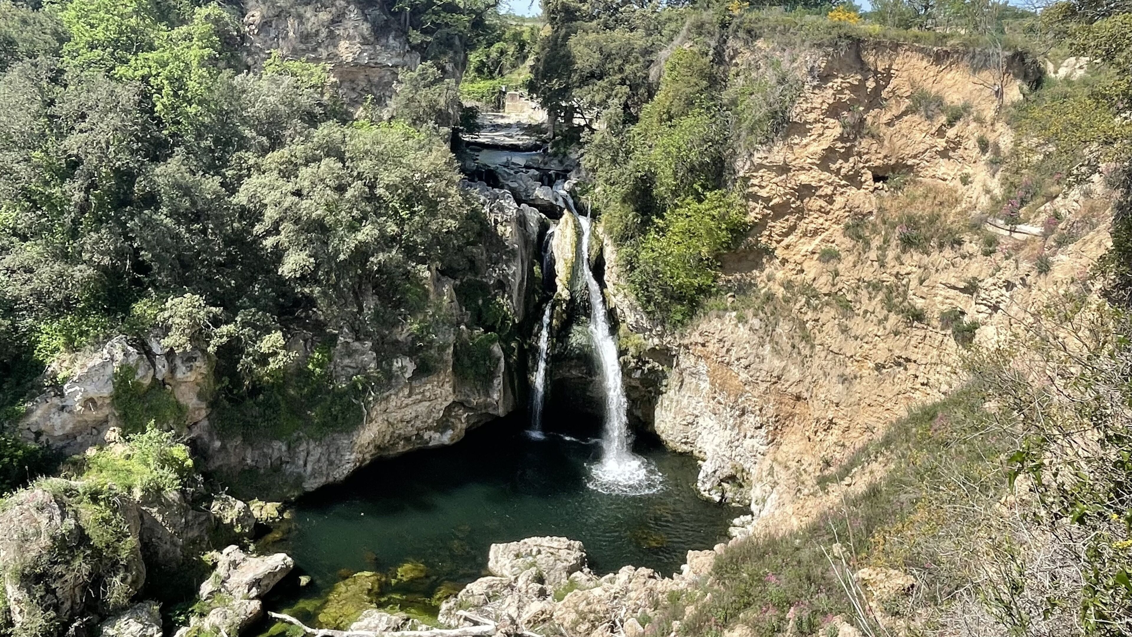 Una cascata che si getta in una pozza limpida, circondata da pareti rocciose e vegetazione rigogliosa.