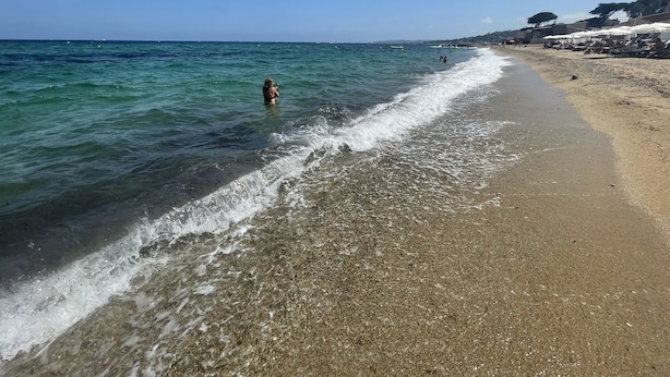 A beach with clear water, a sandy shore, and a few people.