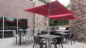 Een terras buiten met tafels, stoelen, een rode parasol en een stenen muur.