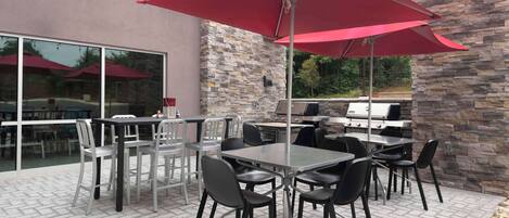 An outdoor patio with tables and chairs, a red umbrella, and a stone wall.