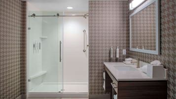 Un baño moderno con ducha de vidrio, tocador con espejo y papel tapiz estampado.