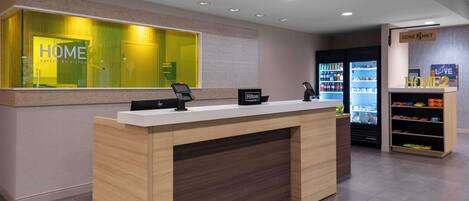 A hotel reception desk with a modern design, a minibar, and a self-service beverage machine.