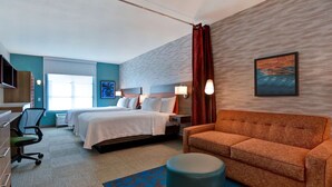 Een hotelkamer met twee bedden, een bank, een bureau met stoel, een televisie en een raam met gordijnen.