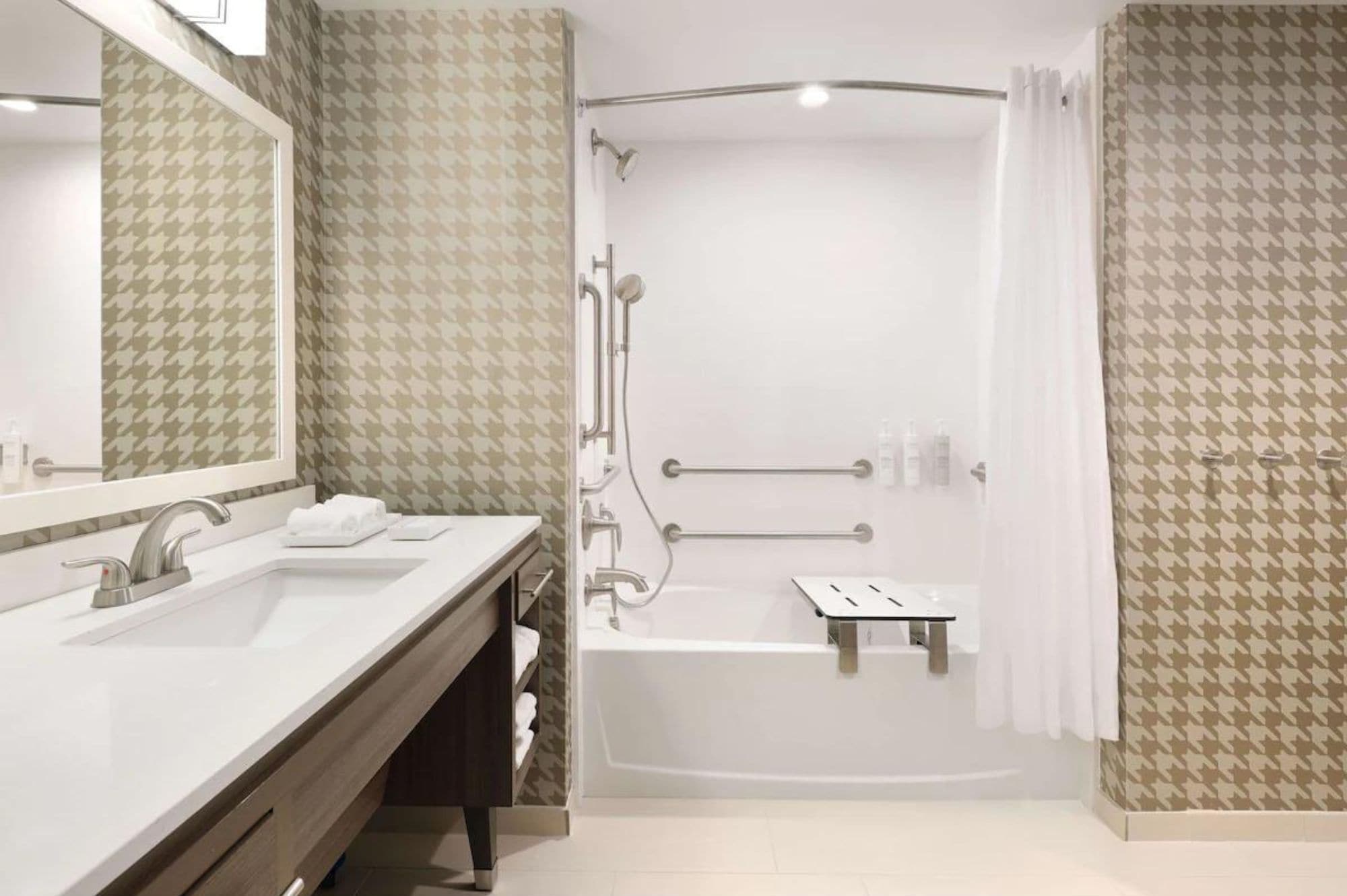 Un baño moderno con tocador doble lavamanos, ducha con barras de apoyo y bañera.