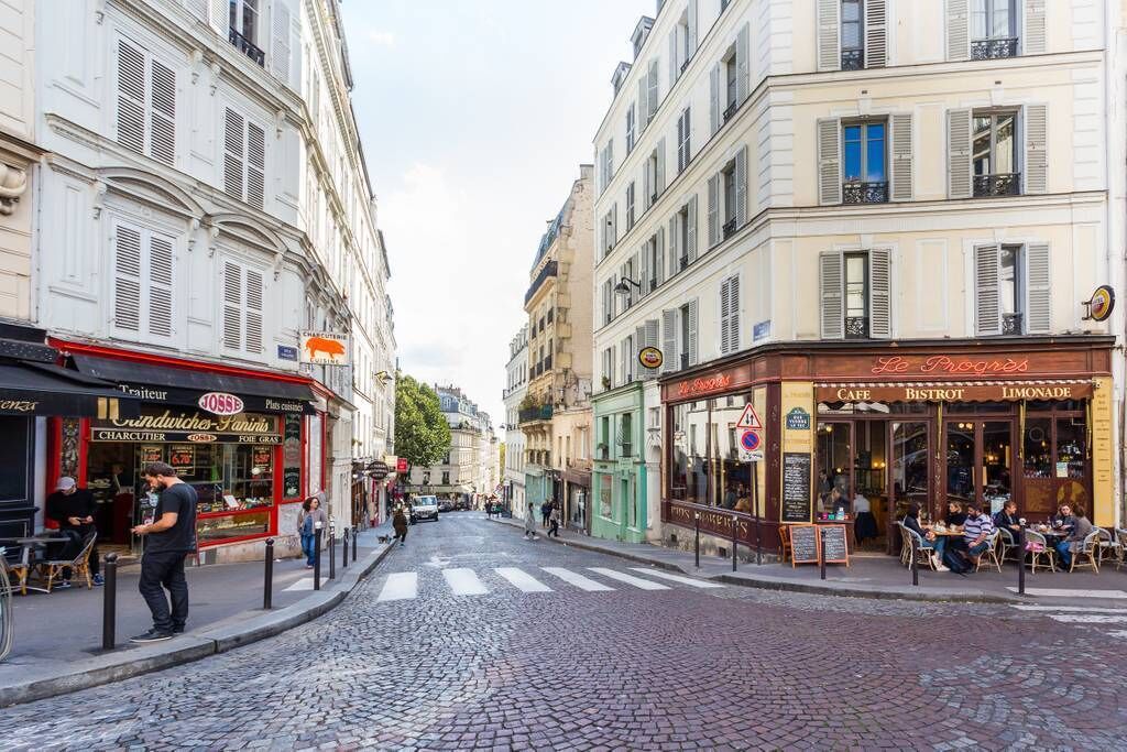 A cobblestone street lined with cafes and shops, including a visible restaurant named 'Le Progrès'.