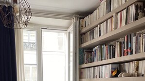 Ein Schlafzimmer mit Bett, Bücherregal, Fenster und einer Pflanze.
