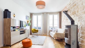 Ein gemütliches Wohnzimmer mit Kamin, einer Couch, einem gelben Sessel und einer Küchenzeile mit Schränken und einer Lampe.