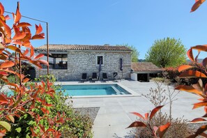 A stone building with a swimming pool, outdoor seating, and a clear blue sky.
