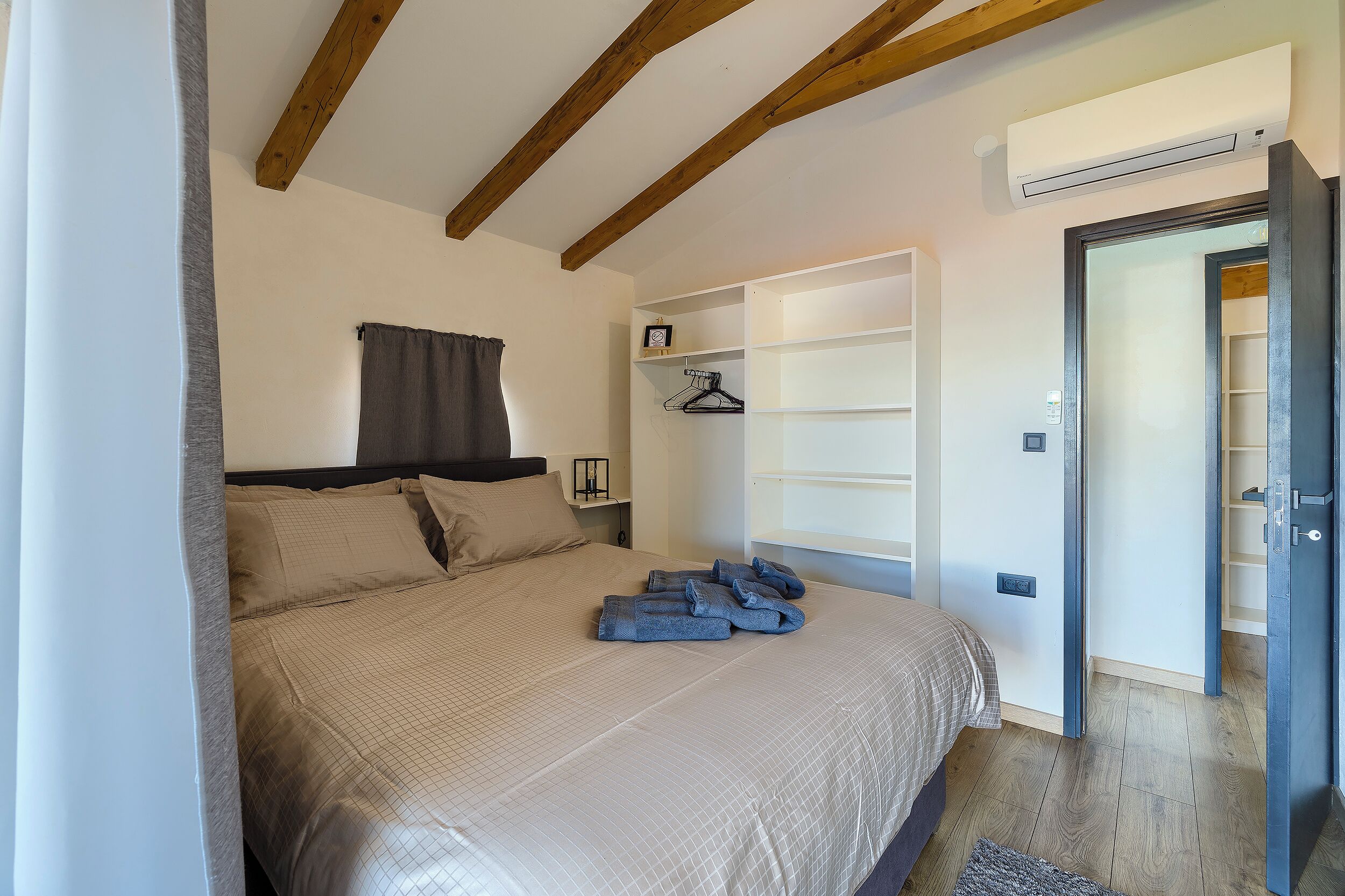 A bedroom with a bed, a wardrobe, a hanging shelf, and an air conditioning unit.